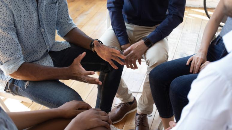 group sitting in a circle in discussion, touching hands