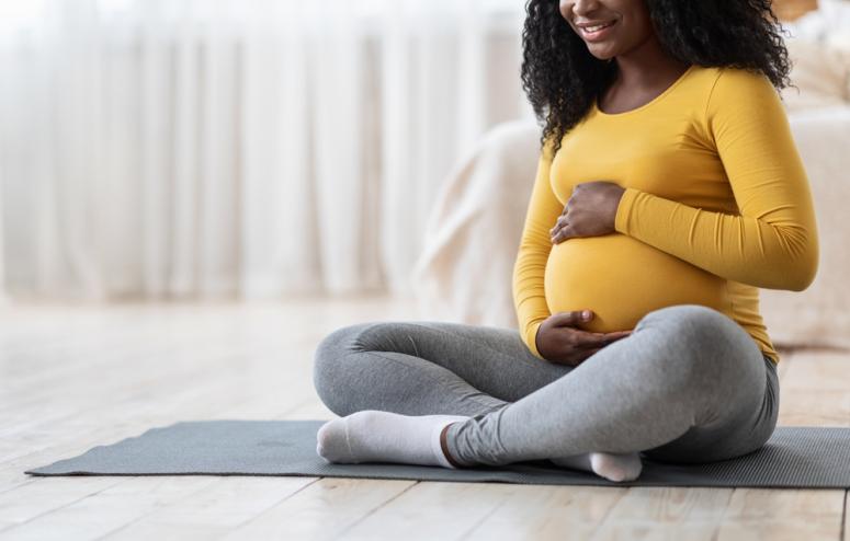 Black pregnant woman on a yoga mat holding her belly