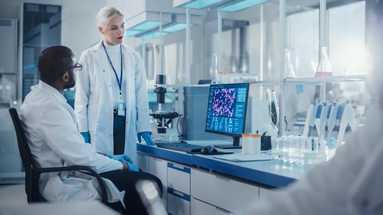 group of researchers in a lab wearing white coats and standing in front of a microscope and computer