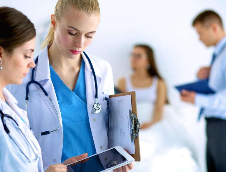 group of doctors in white coats holding a clip board and standing in front of a patient