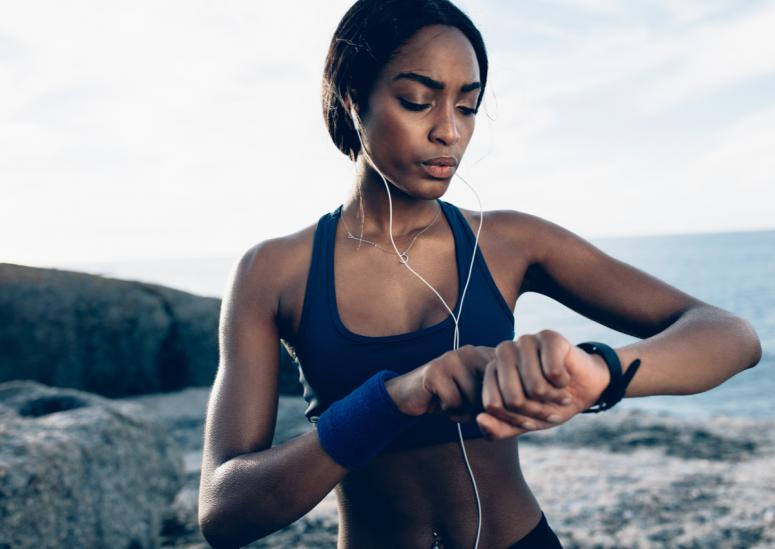 Fit female runner using smart watch to monitor her performance. African Woman setting fitness app on her smartwatch before running session.