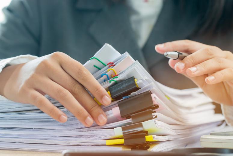 two hands with unfinished stack of document papers with pen