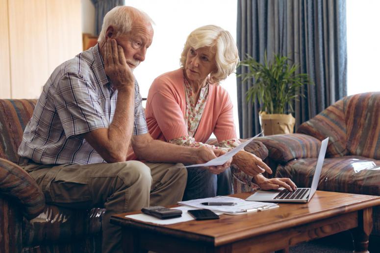 Front view of Caucasian senior couple discussing bill at retirement home. Senior male looks very worried.