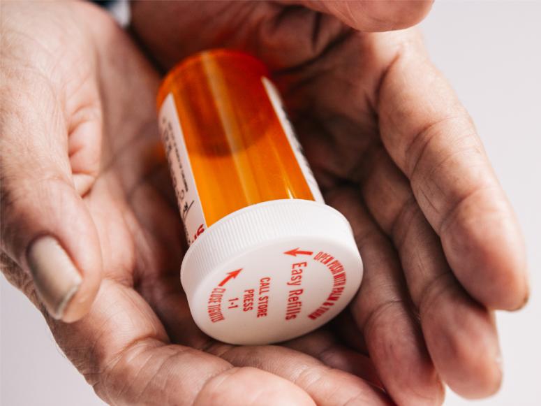 Wrinkled old lady hands holding a bright red orange prescription medication pill bottle.